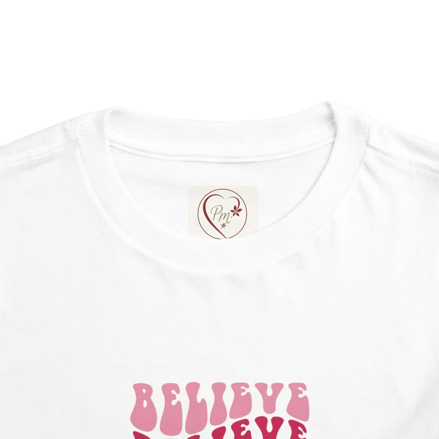 White t-shirt with pink 'BELIEVE' text and a PM Creations 25 logo on a white background