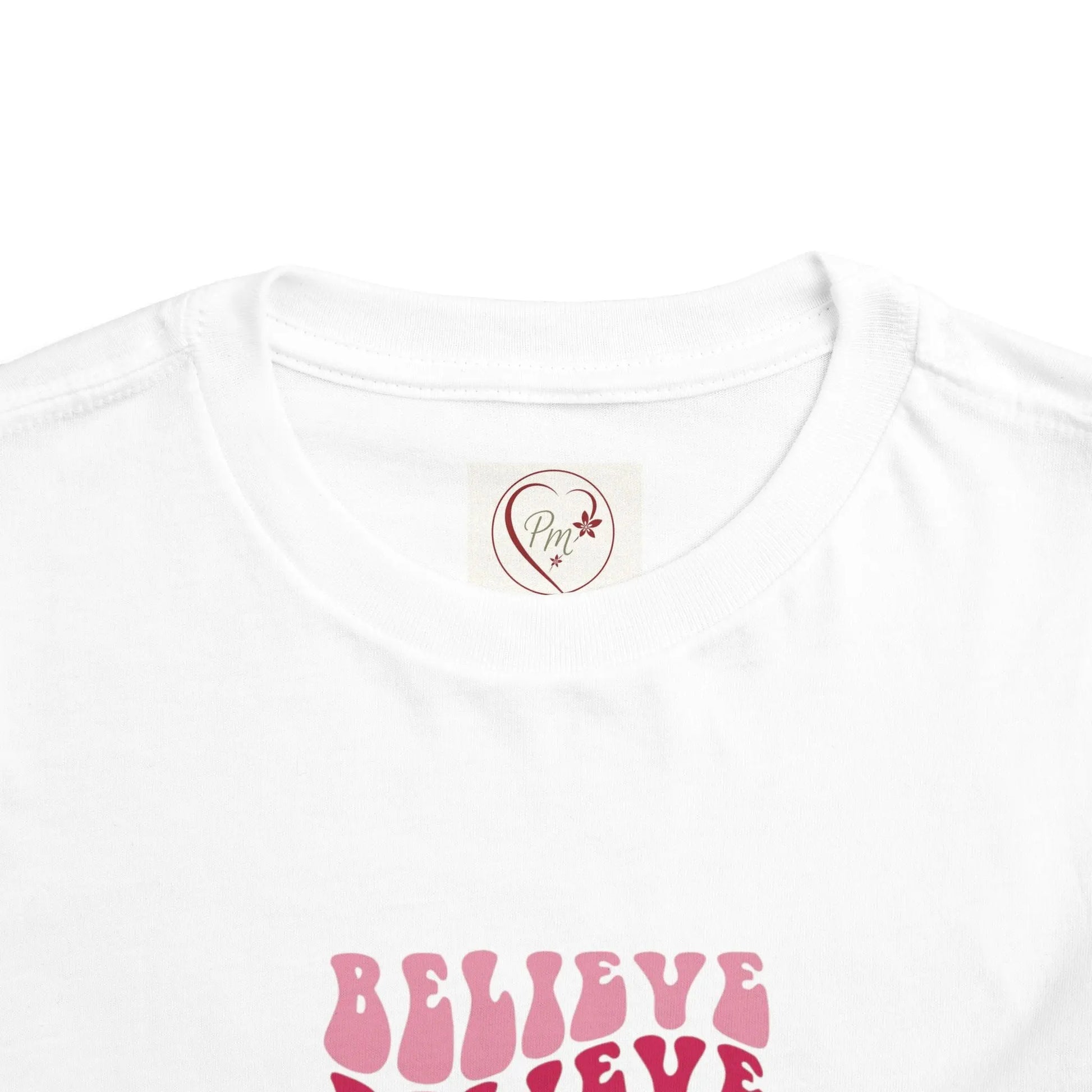 White t-shirt with pink 'BELIEVE' text and a PM Creations 25 logo on a white background