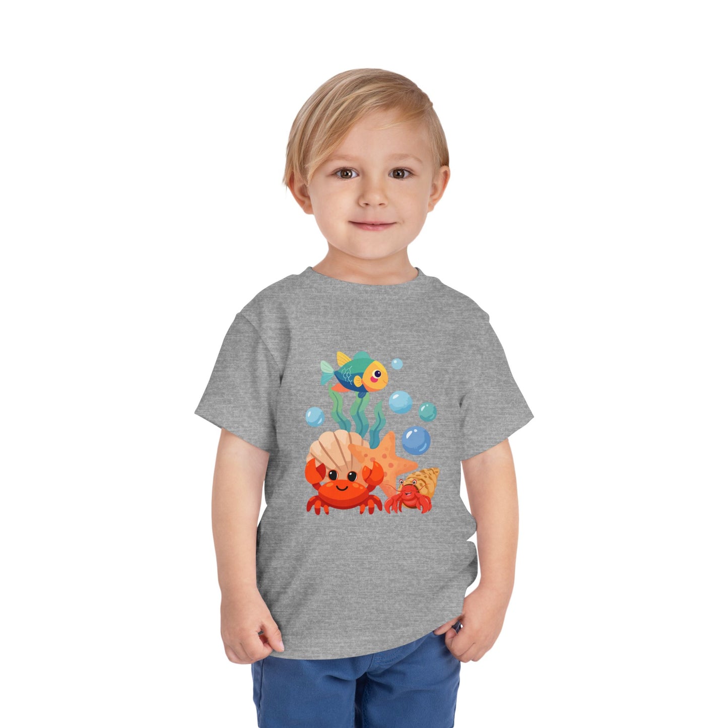 Child wearing an Athletic Heather t-shirt with a colorful fish design on a white background. Playful toddler tee with a crab, fish & shell design. Soft, breathable cotton with tear-away label. Sizes 2T–5T. Perfect for beach days & summer play!