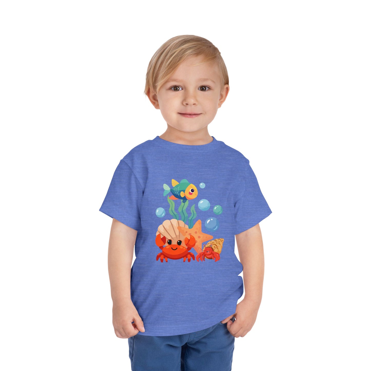 Child wearing a Heather Columbia Blue t-shirt with a colorful fish design on a white background. Playful toddler tee with a crab, fish & shell design. Soft, breathable cotton with tear-away label. Sizes 2T–5T. Perfect for beach days & summer play!