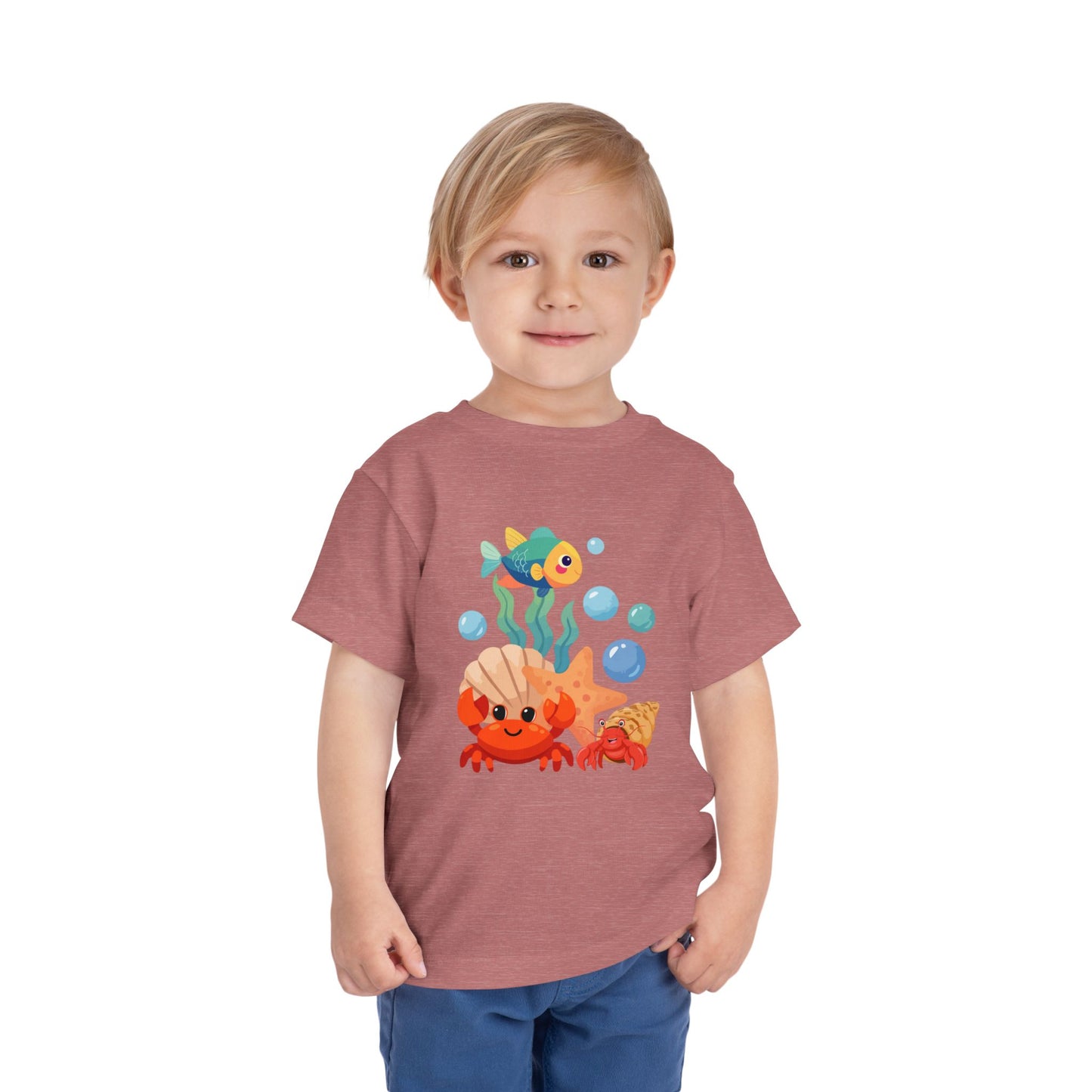 Child wearing a t-shirt with a cartoon design of a fish and a crab on a white background. Playful toddler tee with a crab, fish & shell design. Soft, breathable cotton with tear-away label. Sizes 2T–5T. Perfect for beach days & summer play! Heather Mauve