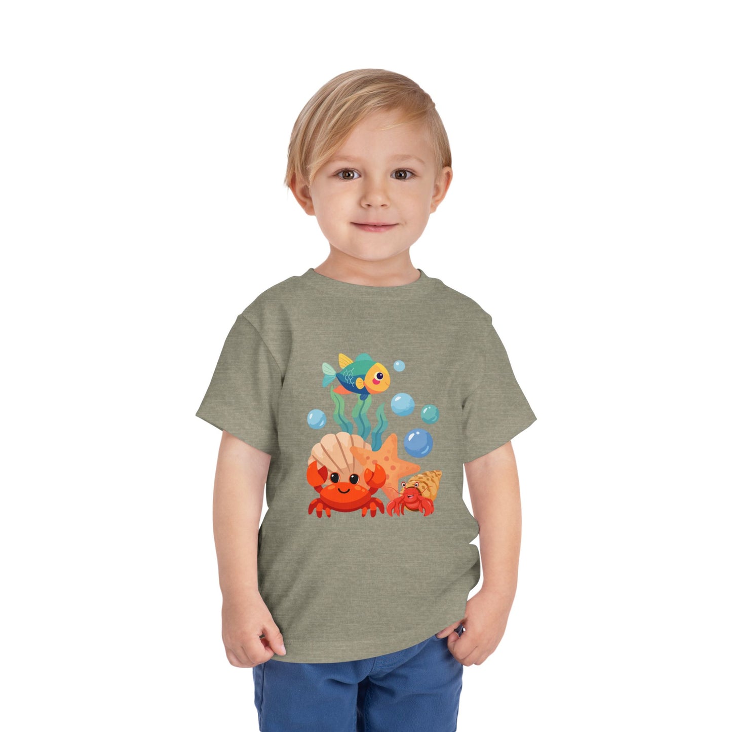 Child wearing a t-shirt with a colorful graphic design on a white background. Playful toddler tee with a crab, fish & shell design. Soft, breathable cotton with tear-away label. Sizes 2T–5T. Perfect for beach days & summer play! Heather Stone