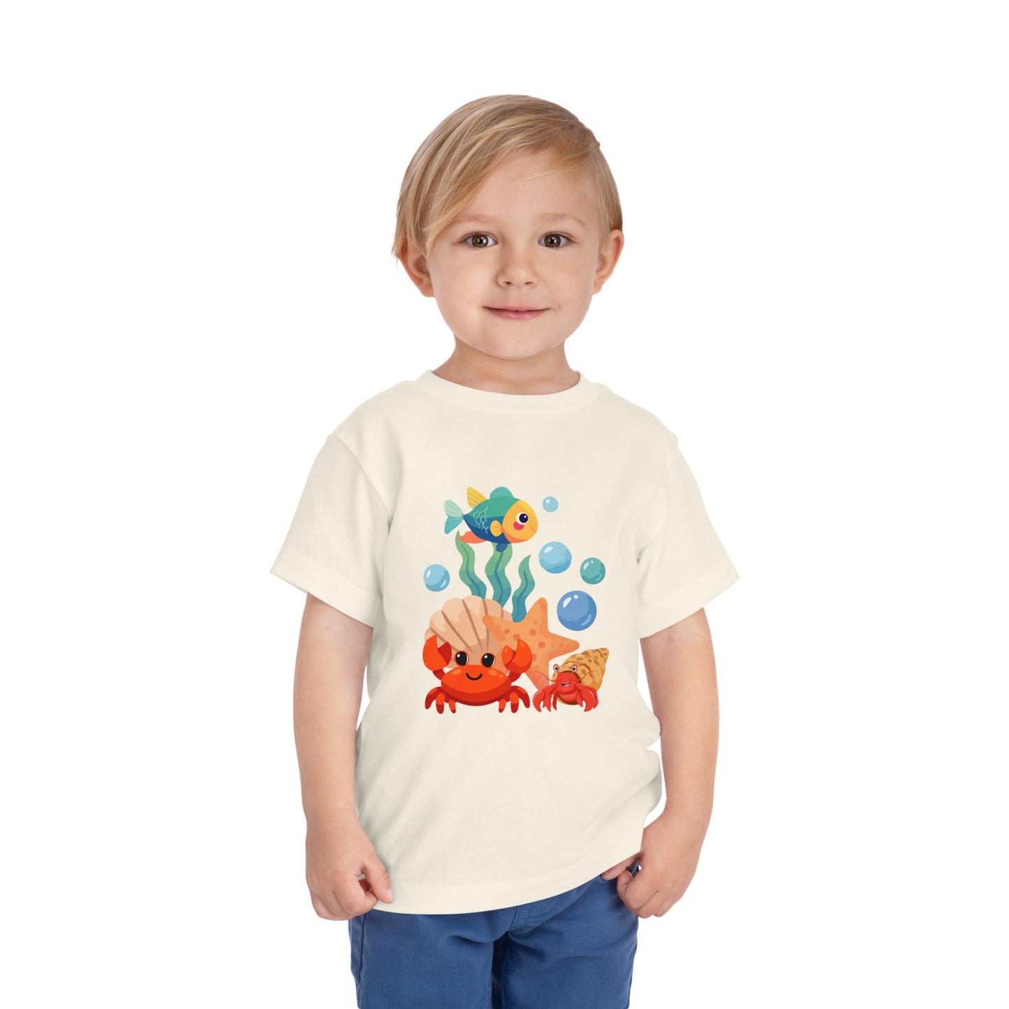 Child wearing a cream t-shirt with a colorful sea-themed design on a white background. Playful toddler tee with a crab, fish & shell design. Soft, breathable cotton with tear-away label. Sizes 2T–5T. Perfect for beach days & summer play! Natural