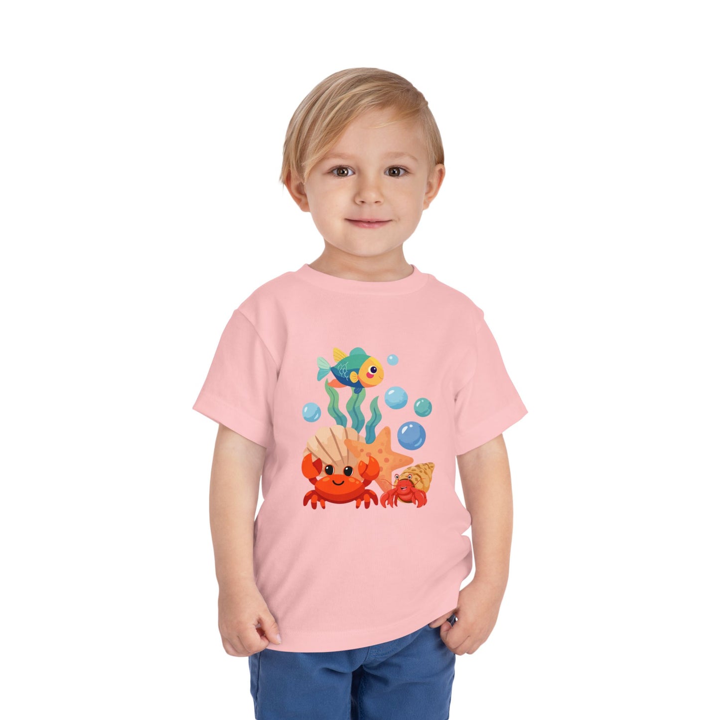 Child wearing a pink t-shirt with ocean-themed graphics on a white background. Playful toddler tee with a crab, fish & shell design. Soft, breathable cotton with tear-away label. Sizes 2T–5T. Perfect for beach days & summer play! Pink