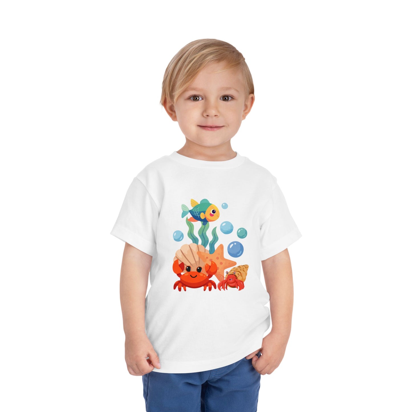 Child wearing a White t-shirt with a colorful fish design on a white background. Playful toddler tee with a crab, fish & shell design. Soft, breathable cotton with tear-away label. Sizes 2T–5T. Perfect for beach days & summer play!