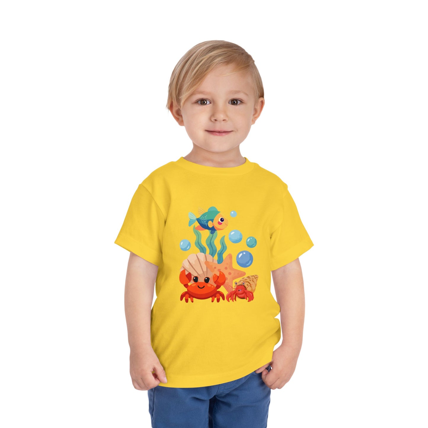 Child wearing a Yellow t-shirt with a colorful sea-themed design on a white background. Playful toddler tee with a crab, fish & shell design. Soft, breathable cotton with tear-away label. Sizes 2T–5T. Perfect for beach days & summer play! 