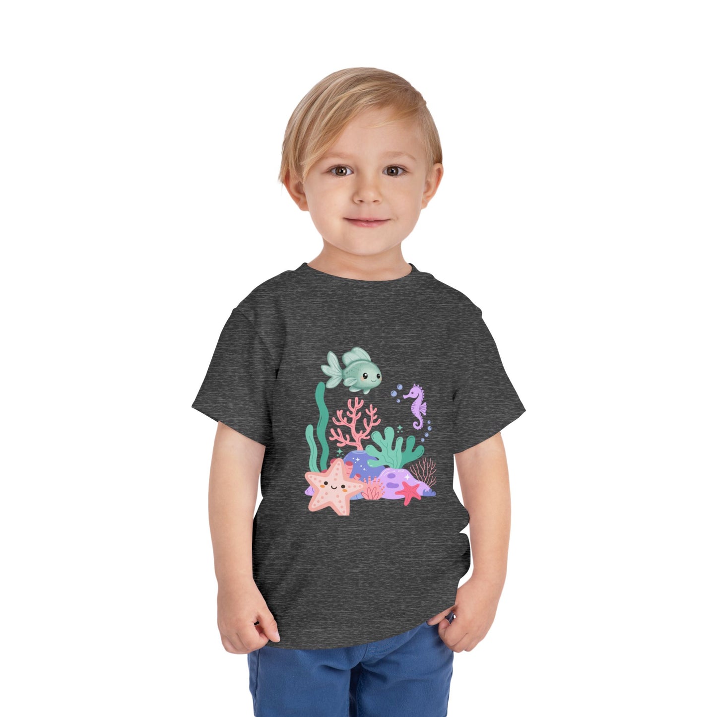 Child wearing a soft, breathable toddler tee featuring pastel sea creatures — fish, seahorse & starfish. Tear-away label, lightweight fabric. Sizes 2T–5T. Shop now! Deep Heather