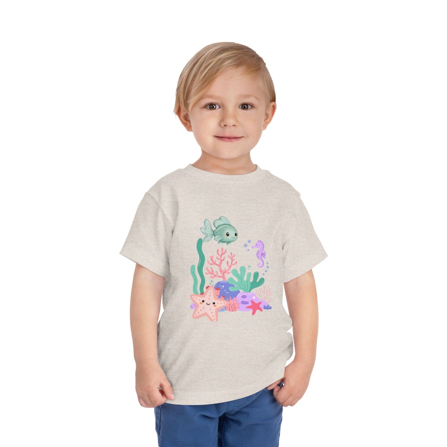 Child wearing a soft, breathable toddler tee featuring pastel sea creatures — fish, seahorse & starfish. Tear-away label, lightweight fabric. Sizes 2T–5T. Shop now! Heather Dust
