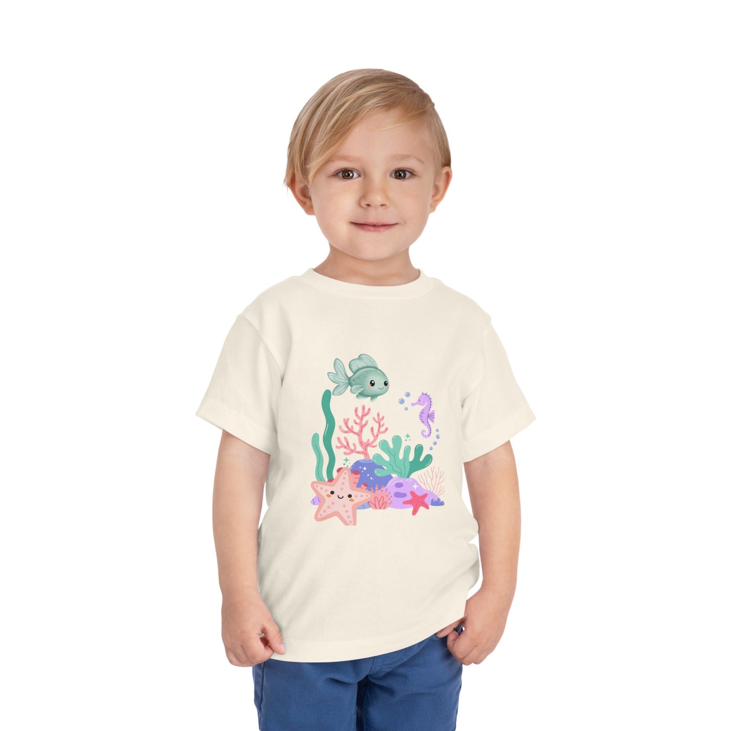 Child wearing a soft, breathable toddler tee featuring pastel sea creatures — fish, seahorse & starfish. Tear-away label, lightweight fabric. Sizes 2T–5T. Shop now! Natural