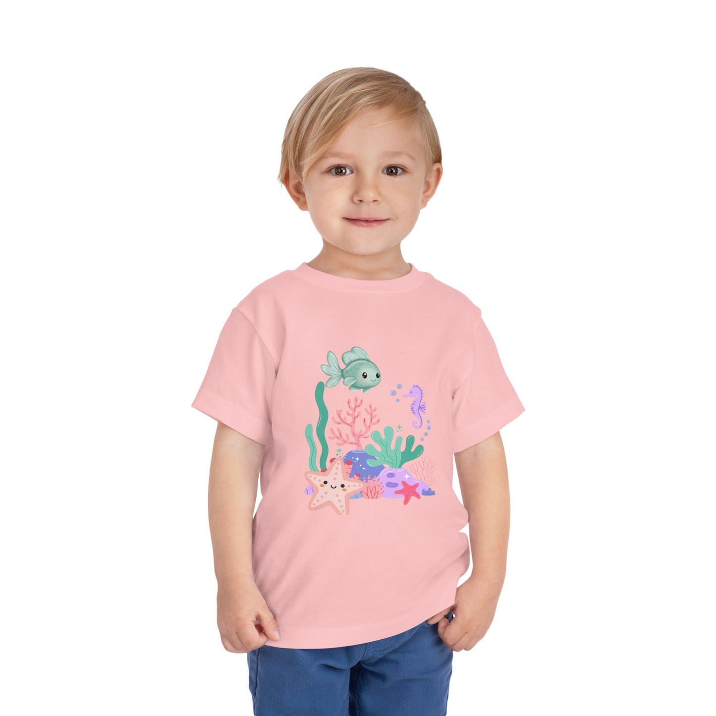 Child wearing a soft, breathable toddler tee featuring pastel sea creatures — fish, seahorse & starfish. Tear-away label, lightweight fabric. Sizes 2T–5T. Shop now! Pink