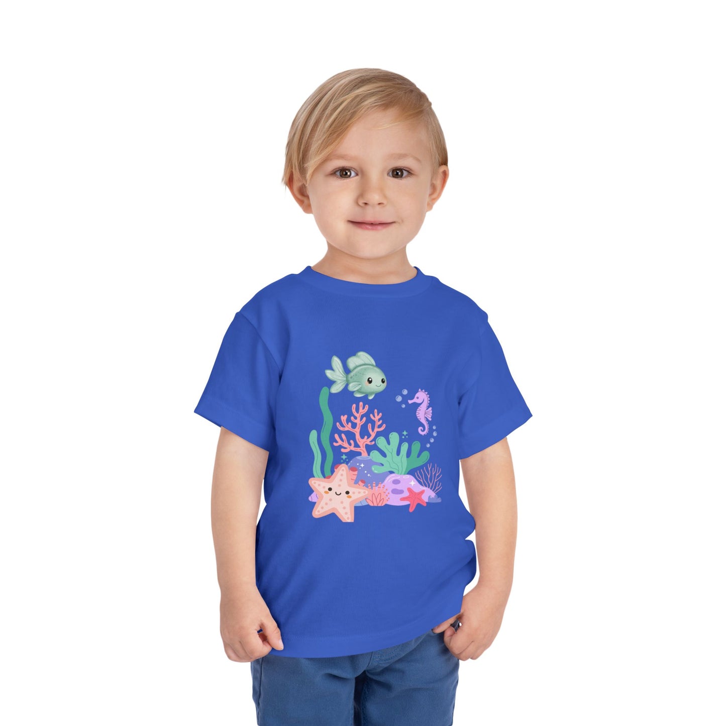 Child wearing a soft, breathable toddler tee featuring pastel sea creatures — fish, seahorse & starfish. Tear-away label, lightweight fabric. Sizes 2T–5T. Shop now! True Royal