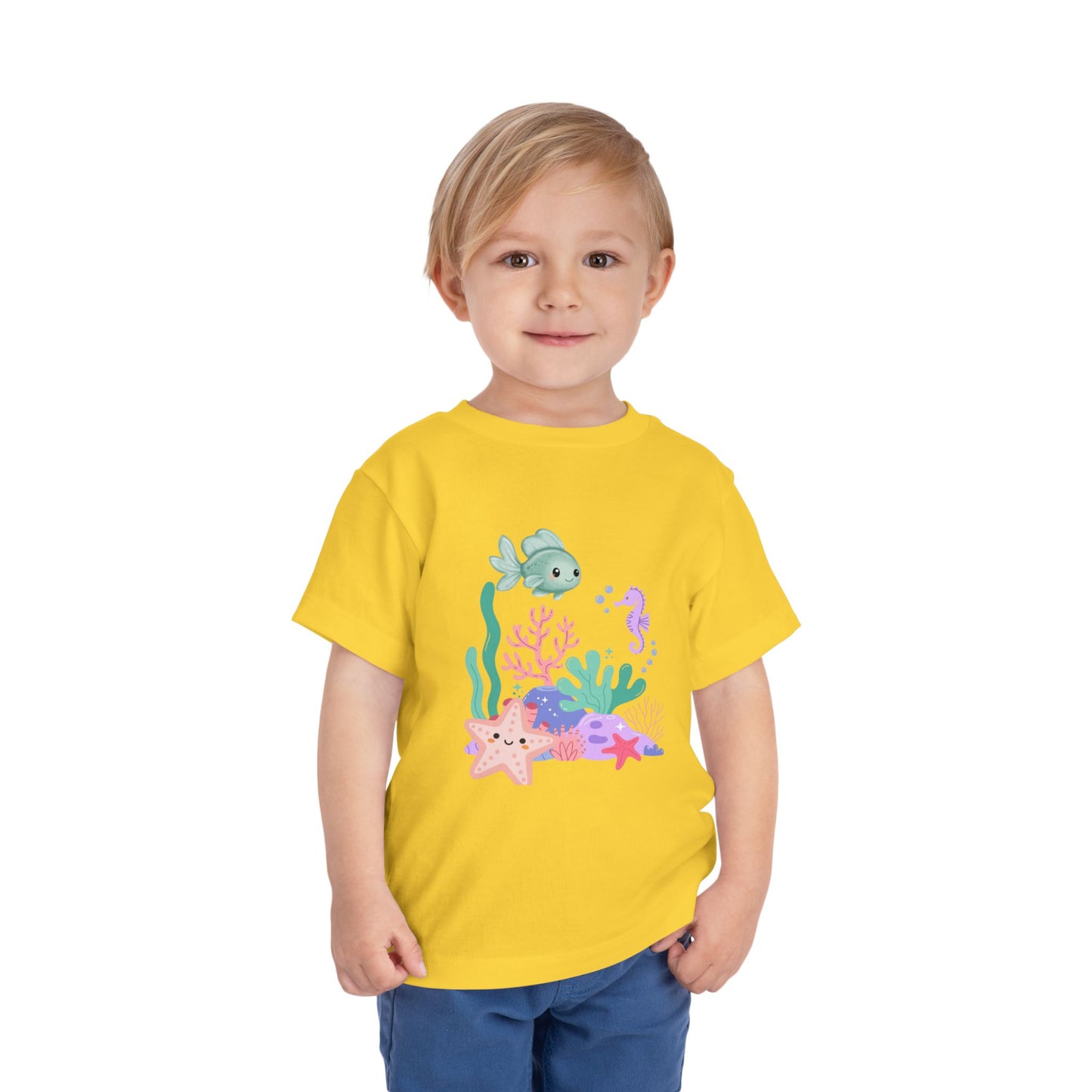 Child wearing a soft, breathable toddler tee featuring pastel sea creatures — fish, seahorse & starfish. Tear-away label, lightweight fabric. Sizes 2T–5T. Shop now! Yellow