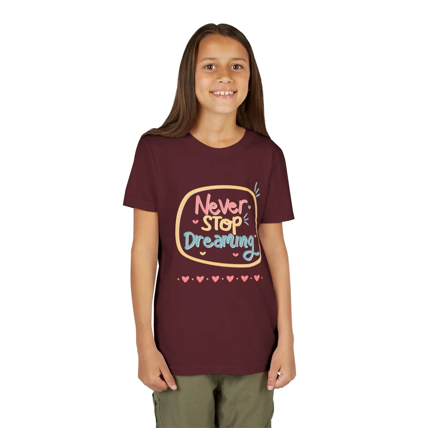 Youth wearing this encouraging youth tee with "Never Stop Dreaming" message. Soft cotton, perfect for school, everyday wear, and inspiring creativity. Motivational kids' clothing. Maroon