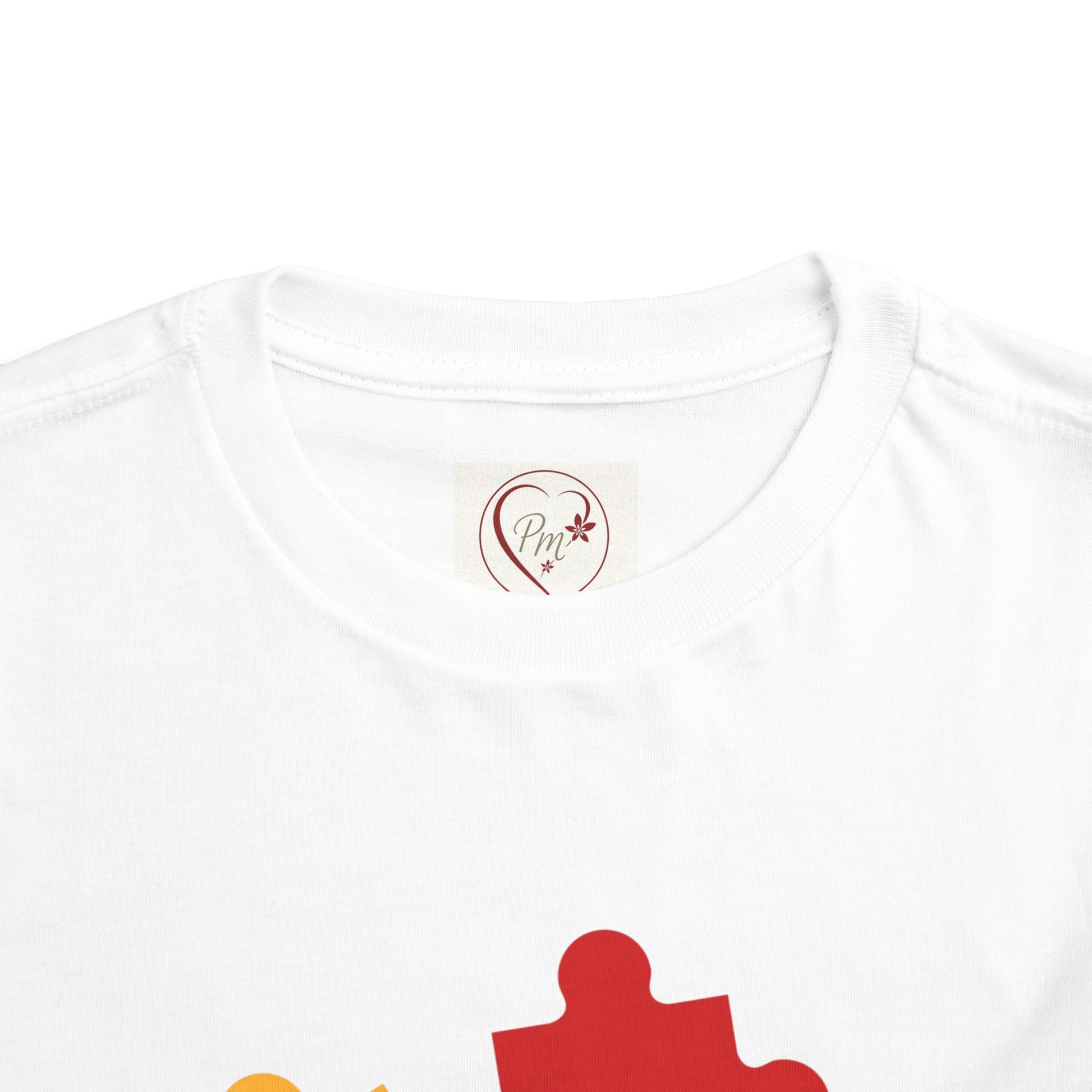 White t-shirt with a red puzzle piece design and a PM Creations 25 logo on the neckline.