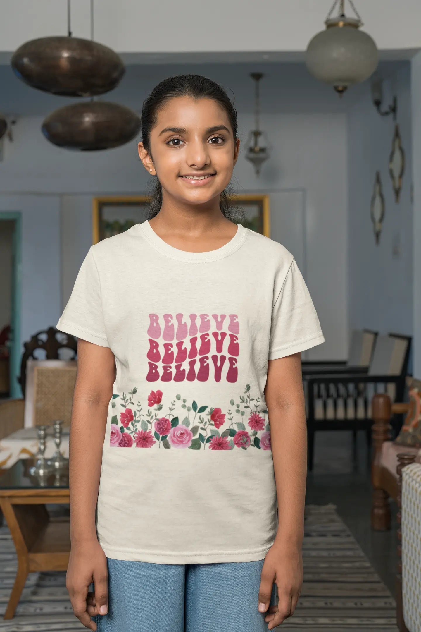 Youth wearing Believe tee with vintage pink text and hand-drawn rose design,
Natural
